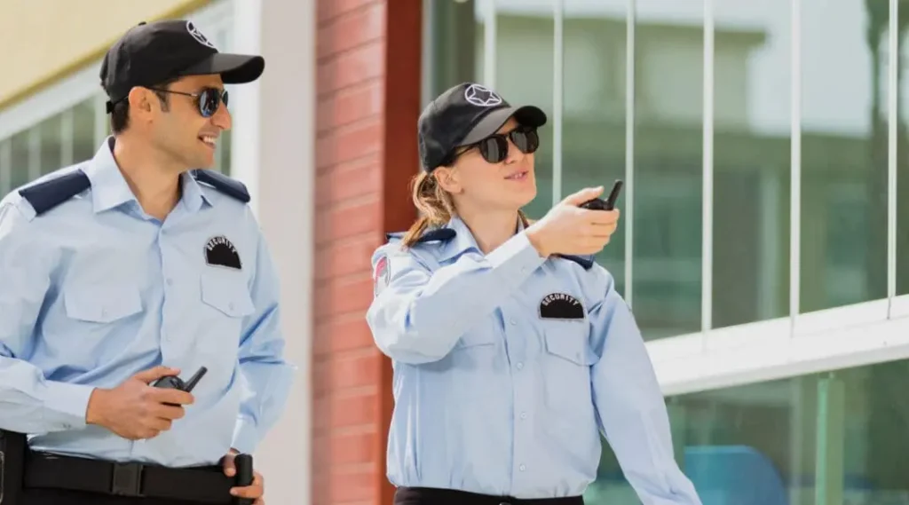 Two security guards in uniform using walkie-talkies outside a building, ensuring public safety.