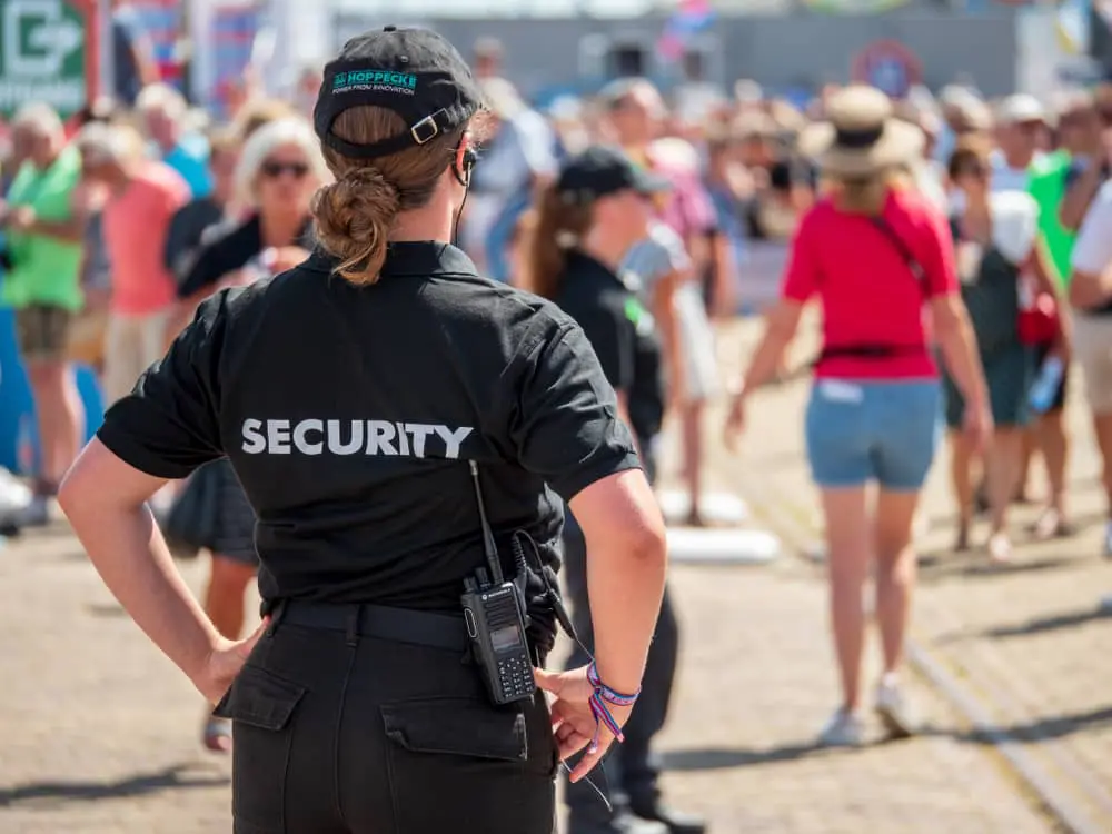 Female security officer monitoring a crowded outdoor event, ensuring safety and crowd control.